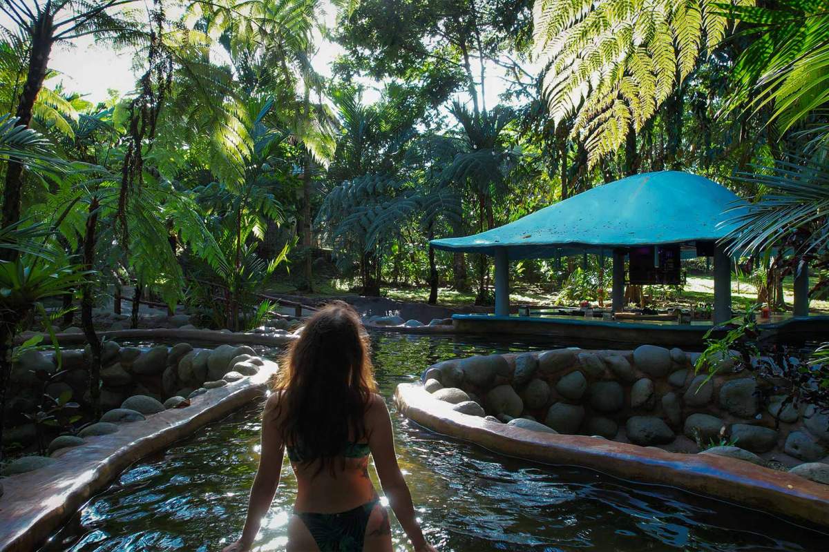 Relaxing scene of a person enjoying the warm thermal waters amidst vibrant green foliage and sunlight at a natural hot spring resort